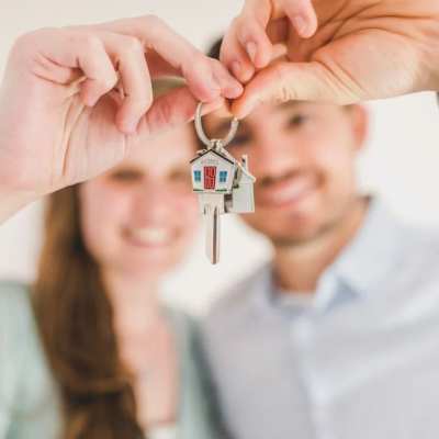 Ein Paar hält einen Schlüssel mit einem kleinen Haus ins Bild