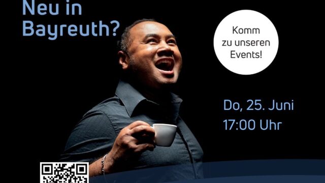 Hinweis auf dem Stammtisch "Neu in Bayreuth". Zusehen ist ein fröhlicher Mensch mit Kaffeetasse vor schwarzem Bühnenhintergrund
